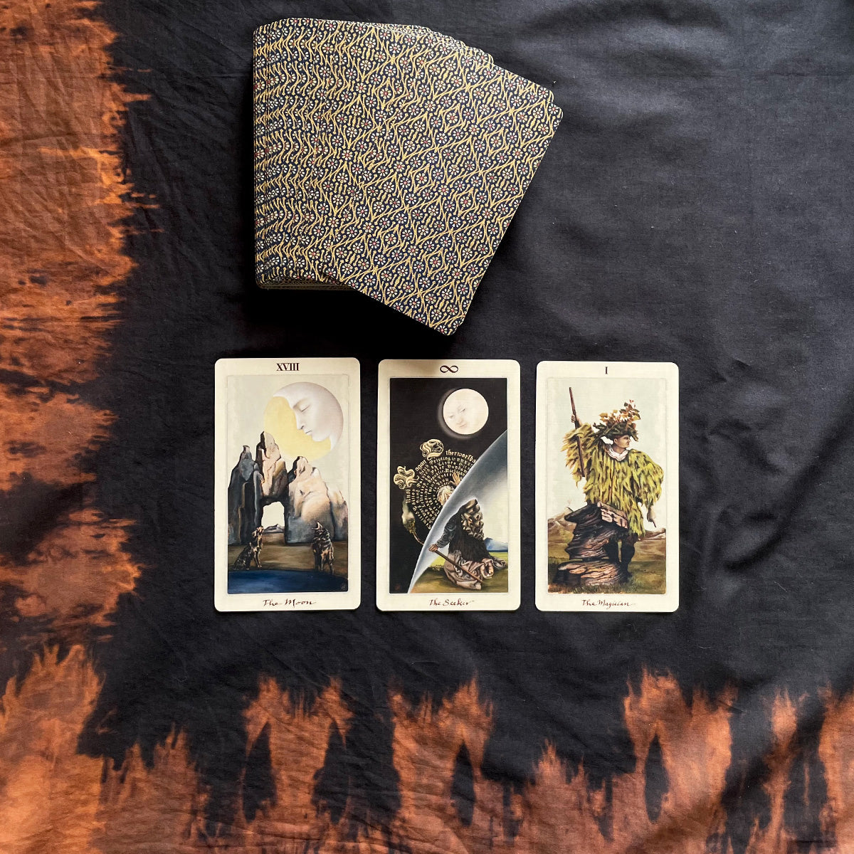 Three tarot cards on a dark fabric surface with a patterned book above them.
