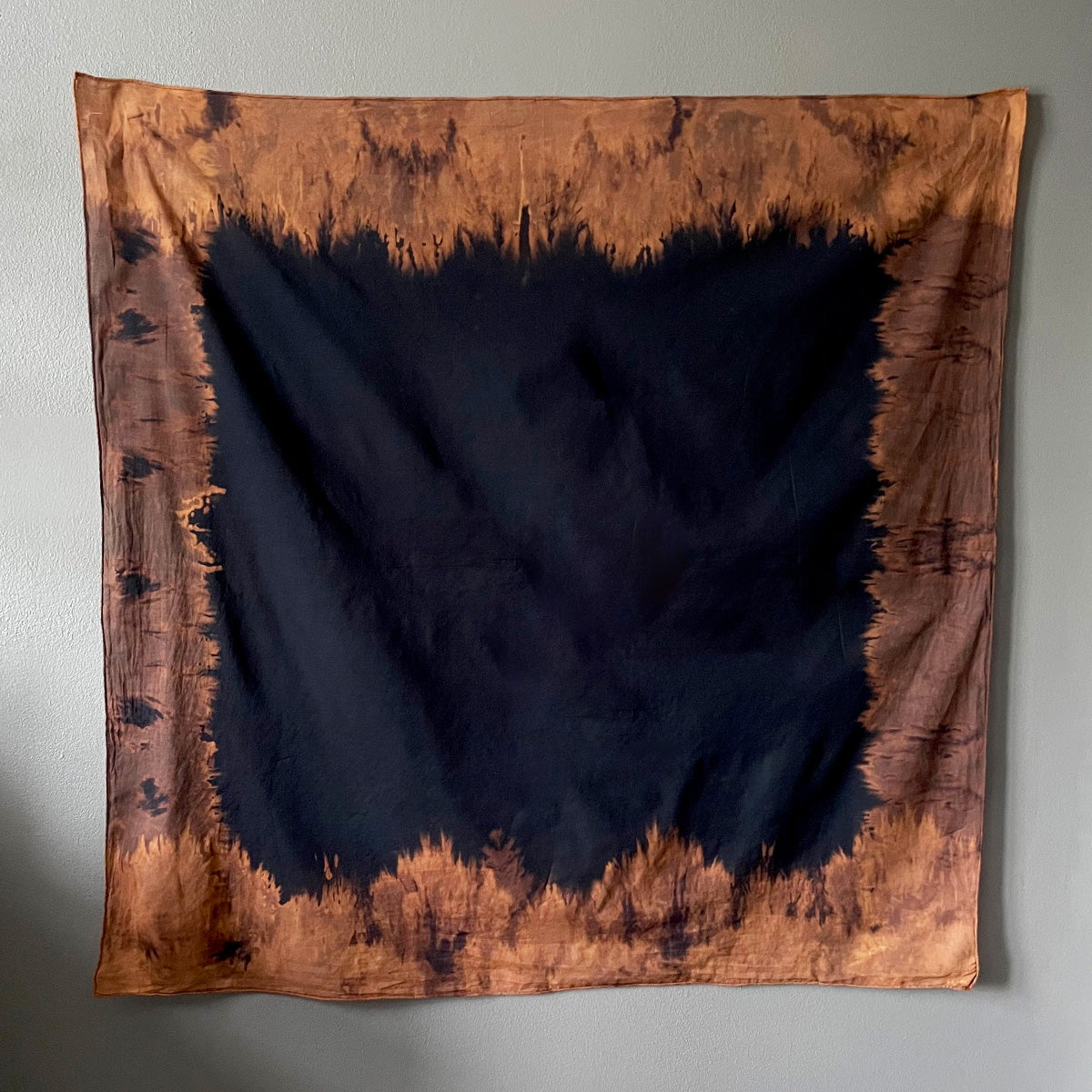 A dark-colored cotton tarot cloth with a lighter border, displayed flat against a light-colored wall.