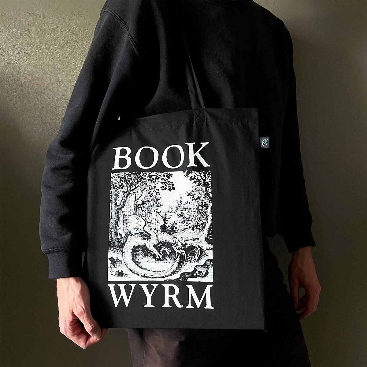 Person holding a black tote bag with 'Book Wyrm' design and text.