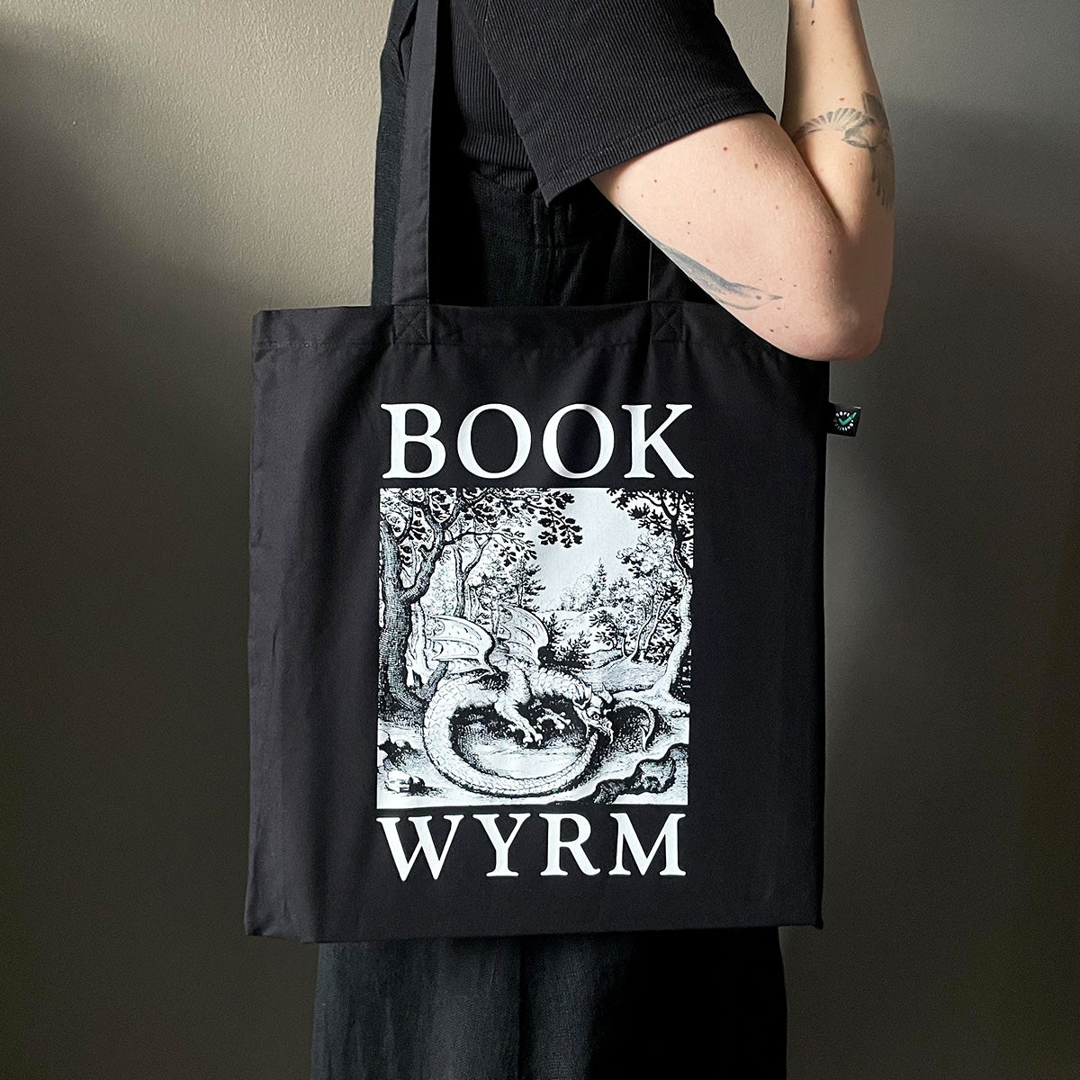 Black tote bag with 'Book Wyrm' design held by a person against a neutral background