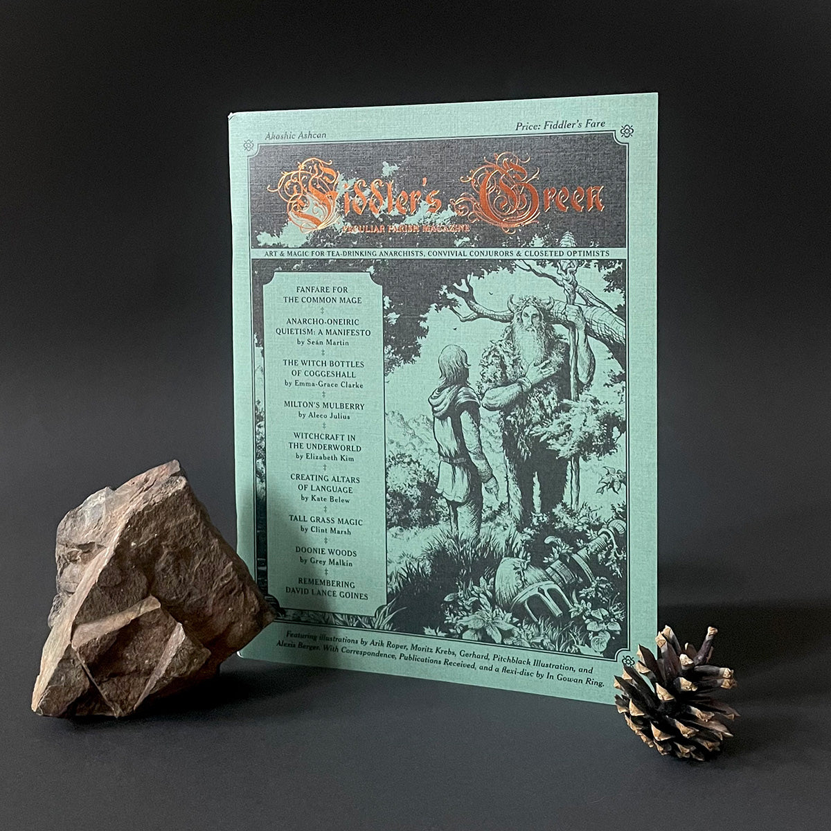Magazine titled 'Fiddler's Green' with a rock and pine cone on a dark background