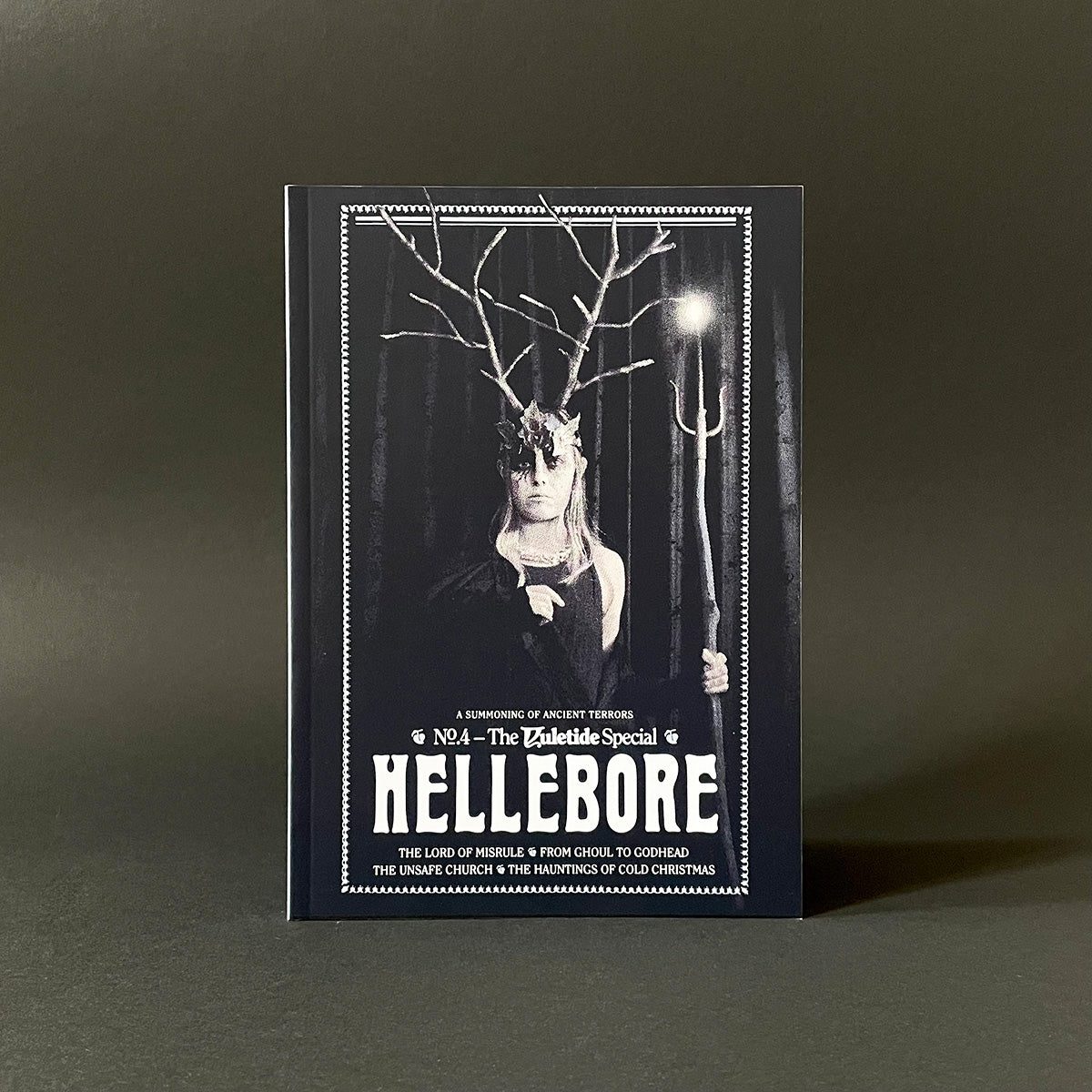 Book titled 'Hellebore' with a dark cover featuring a person with antlers and a pitchfork on a gray background