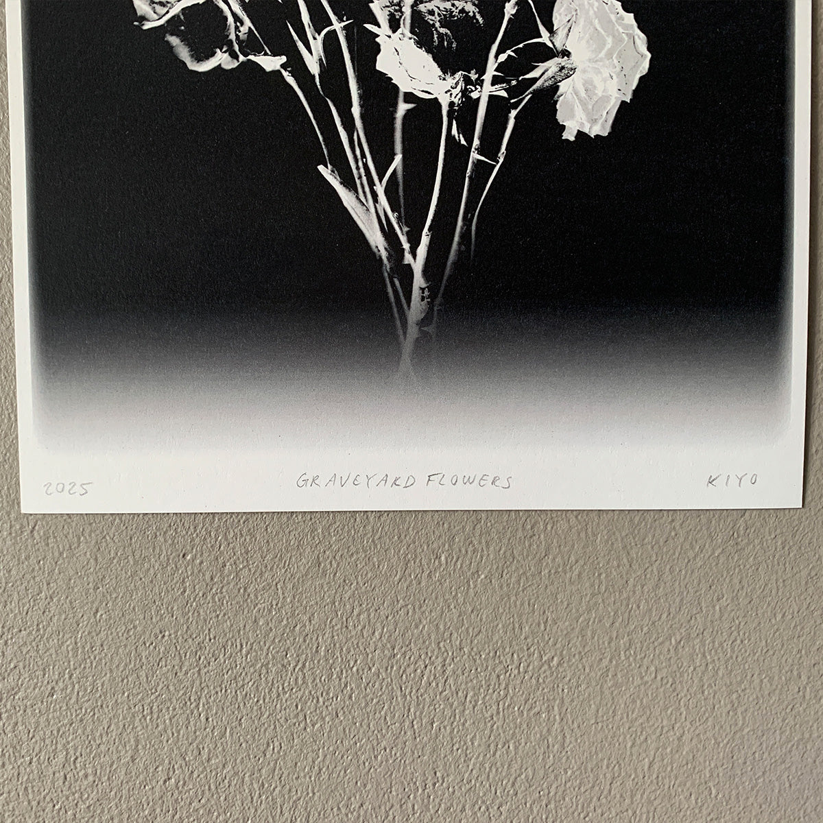 Black and white photograph of 'Graveyard Flowers' by Kiyo on a textured wall.