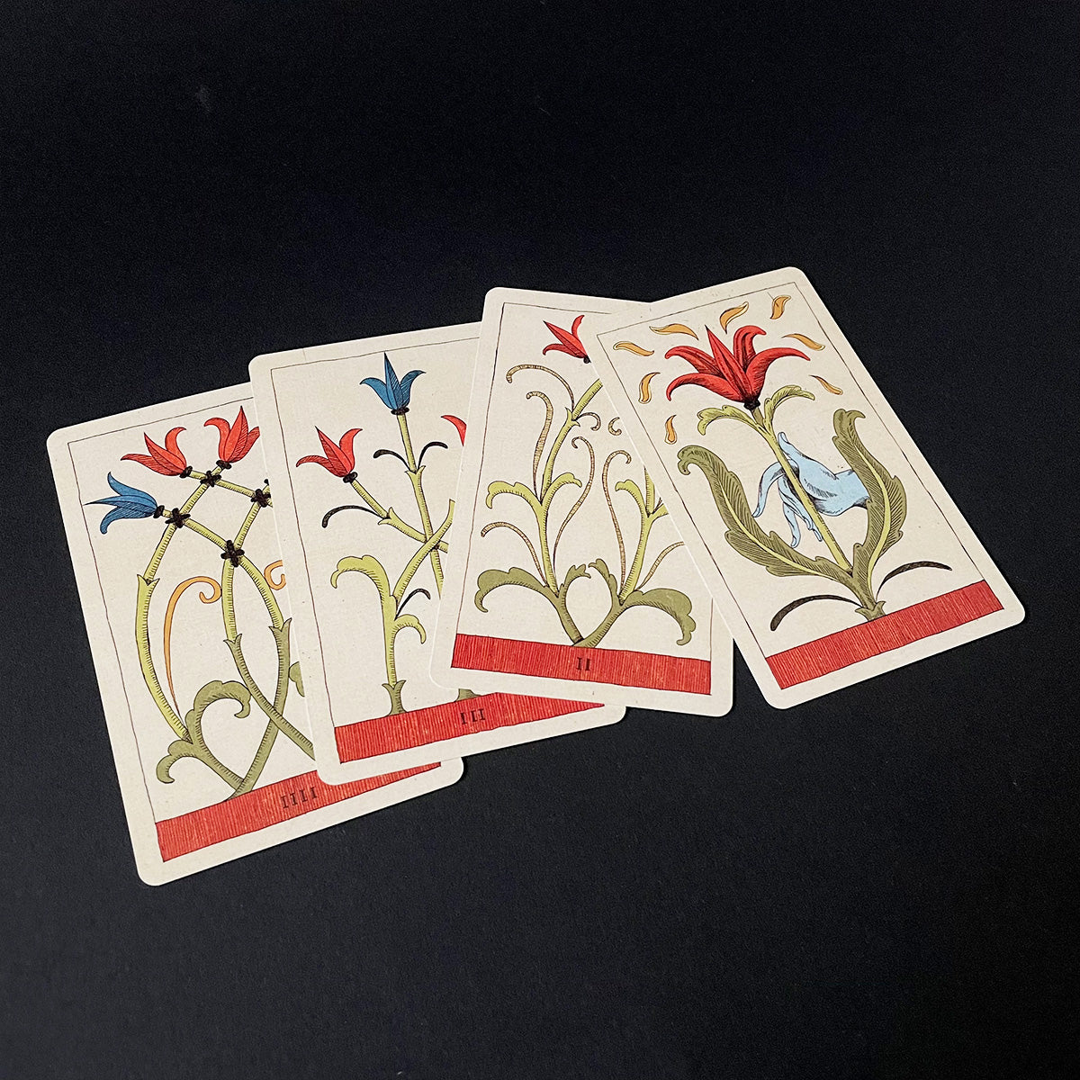 Four playing cards with floral designs on a black background