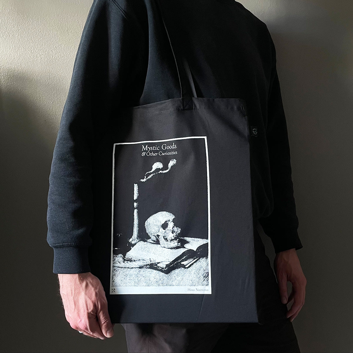 Person holding a black tote bag with a skull design and text.
