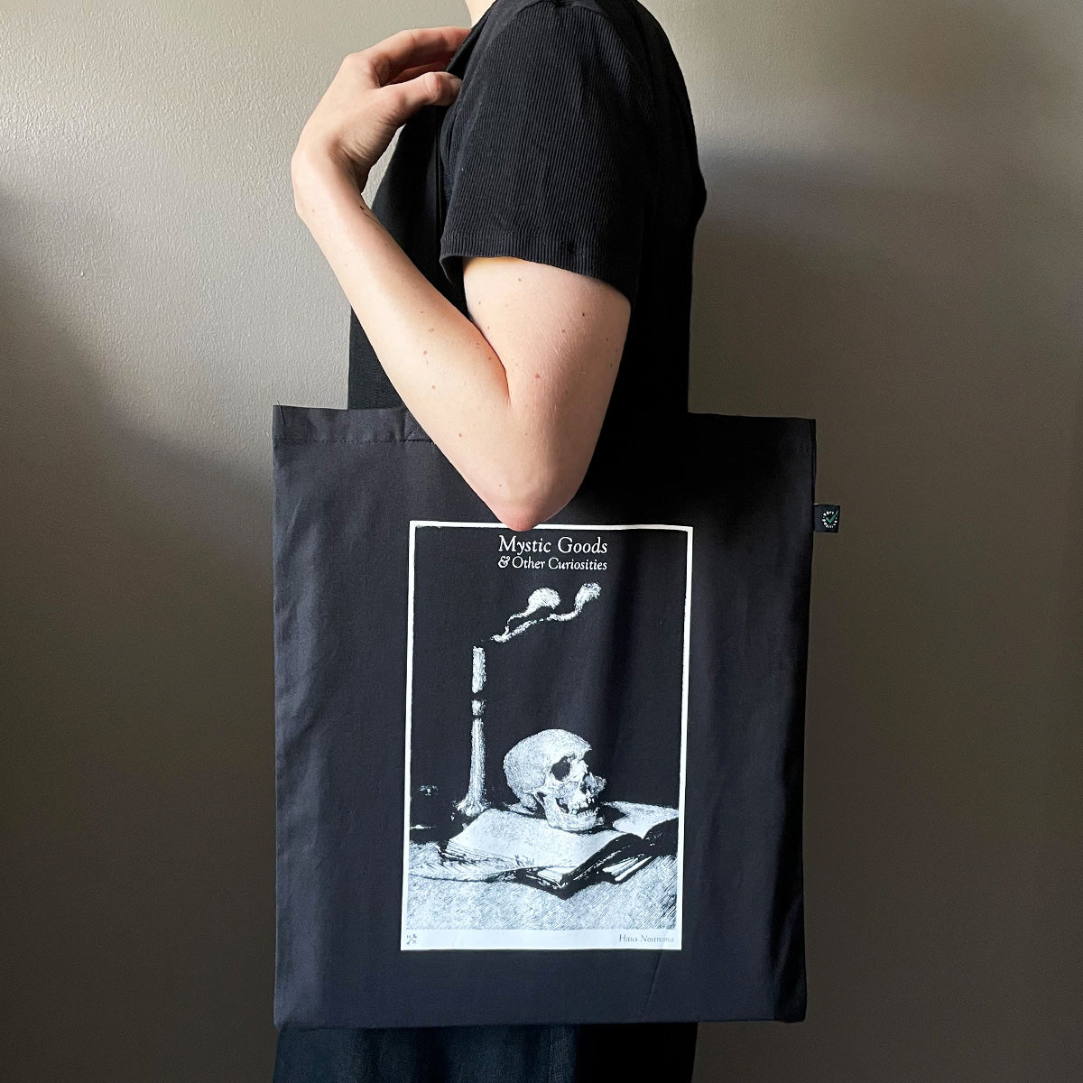 Person holding a black tote bag with a skull and books design on a plain background