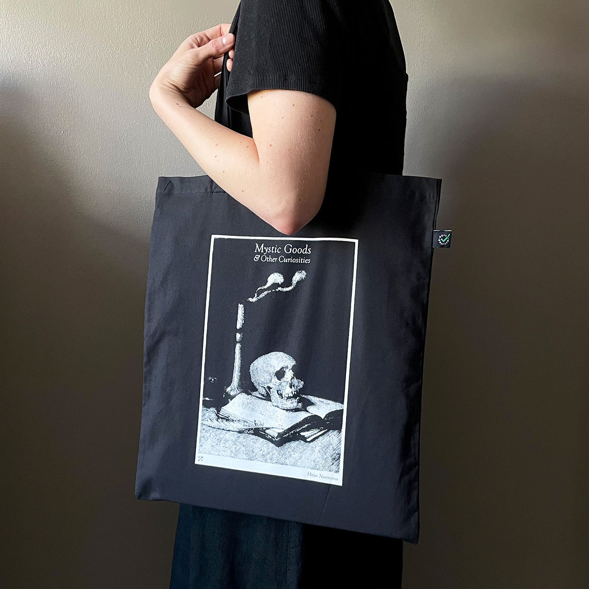 Person holding a black tote bag with a graphic design on a plain background