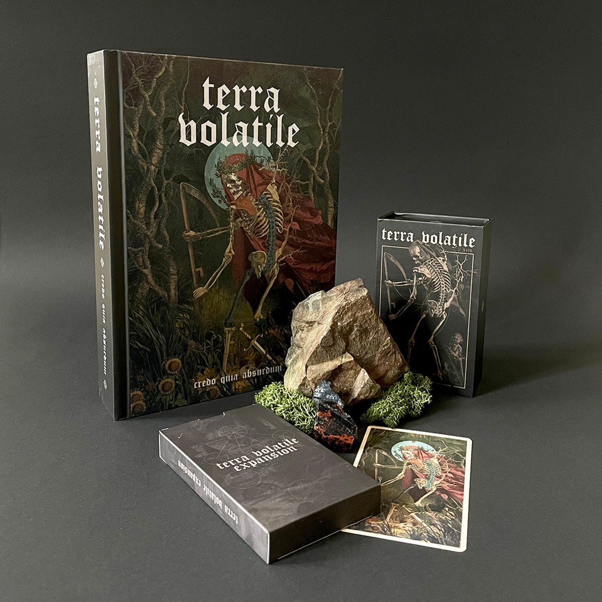 Collection of 'terra volatile' books, cards, and a rock-like object on a dark background