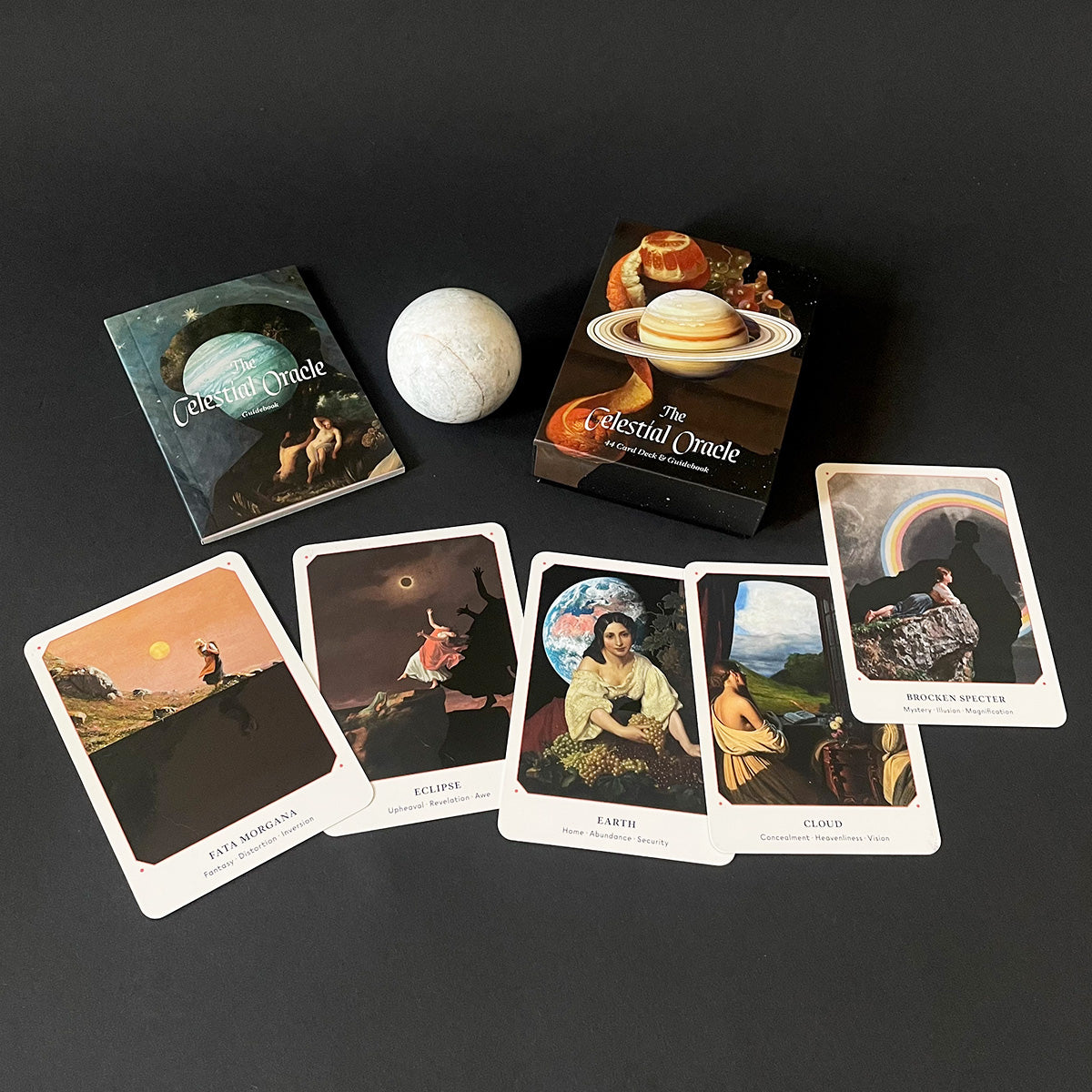 Set of Celestial Oracle cards on a dark surface with a moonstone.