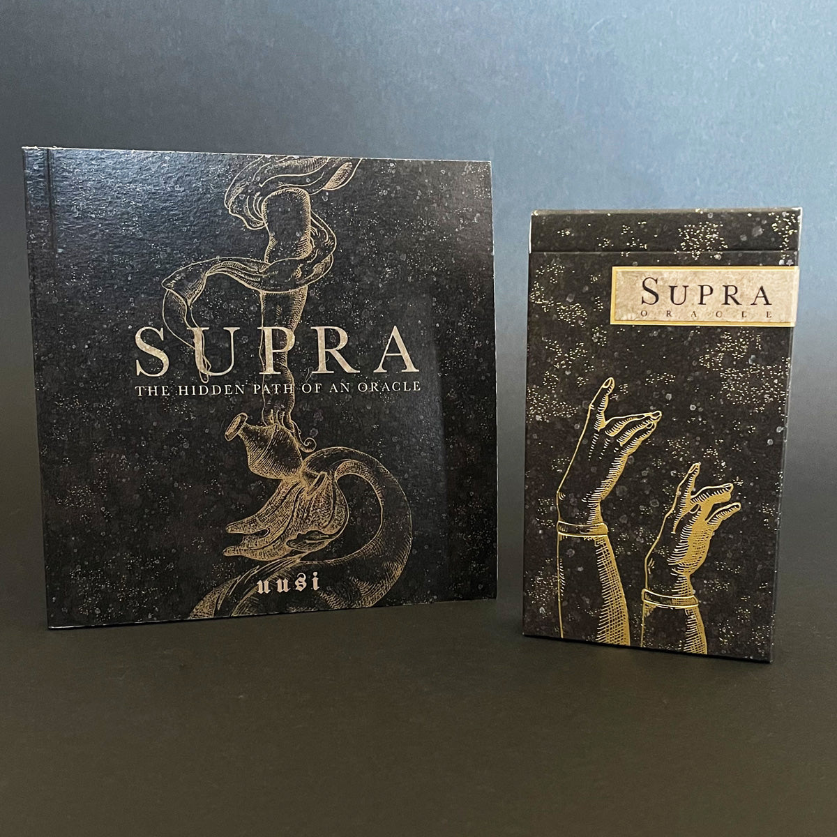 The image shows the Supra Oracle deck and its accompanying book. The deck features a pair of embossed gold hands against a dark background.