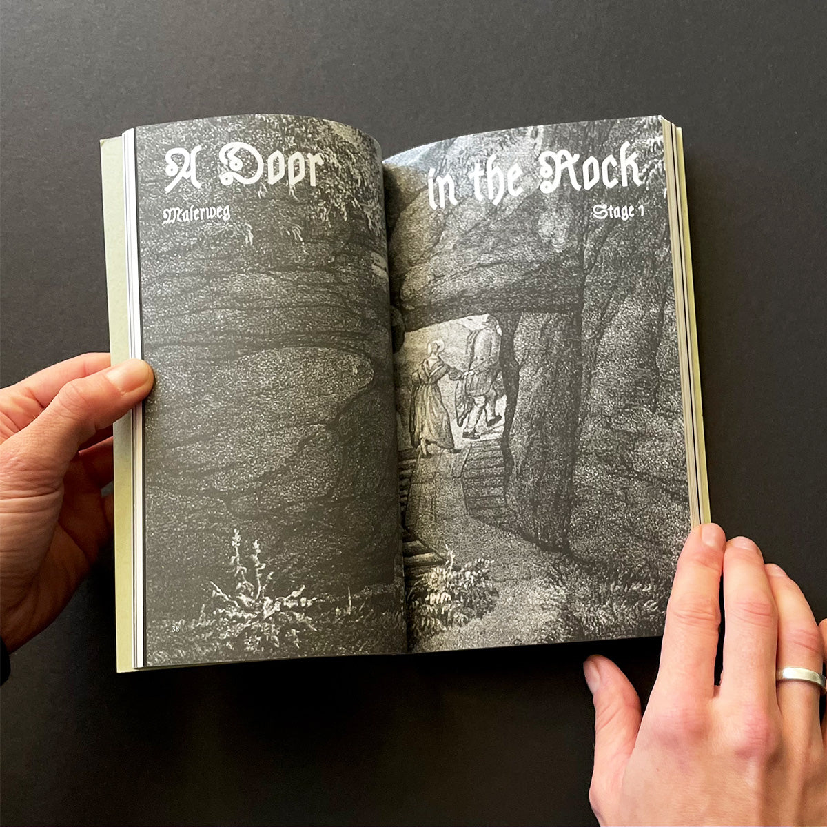 Open book with black and white illustrations held by a person against a dark background