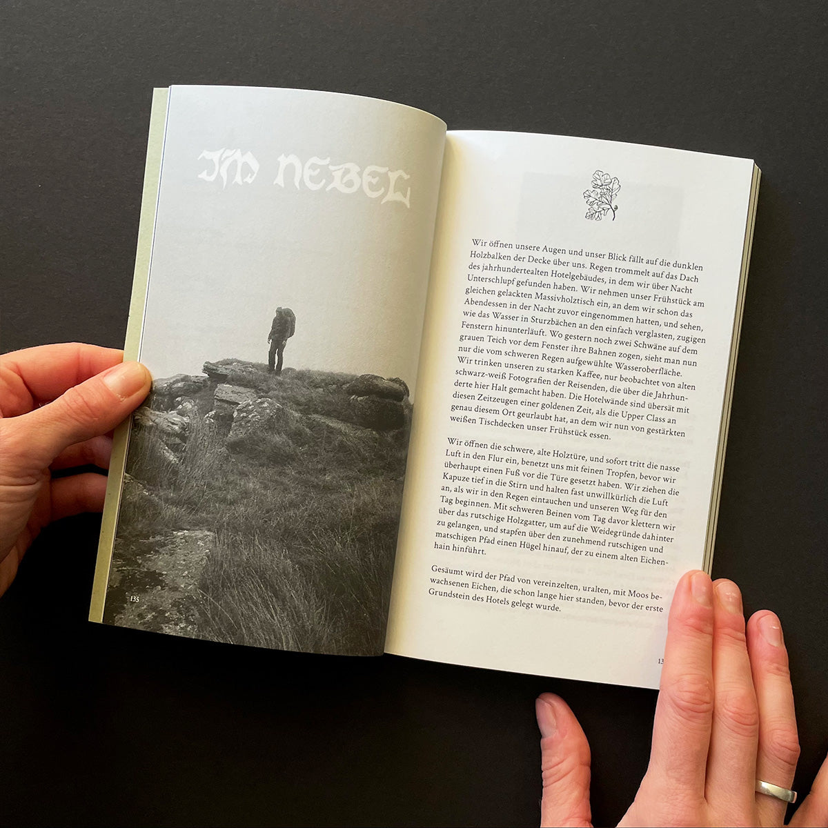 Open book held by hands with a black and white photograph and text on a dark background